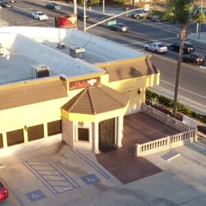 Aerial view of El Baja in Fontana, adjacent parking lot, and nearby road with moving vehicles. The setting sun casts long shadows across the scene.