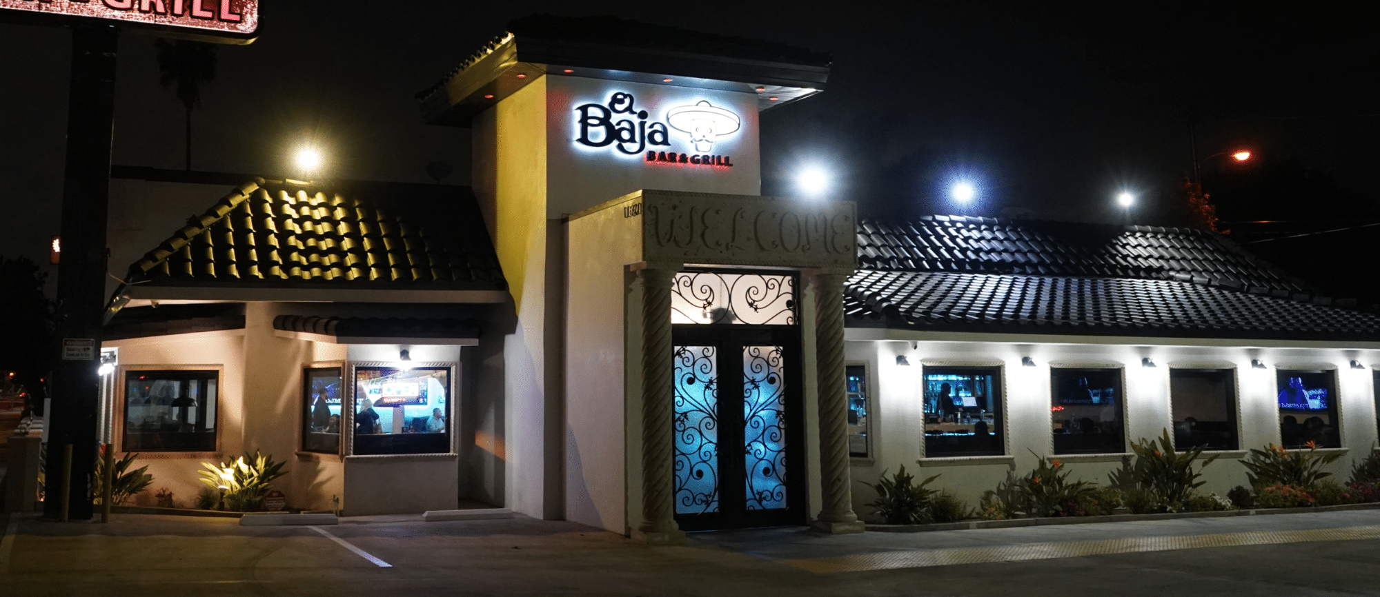 Nighttime view of El Baja Grill, a Mexican food restaurant exterior featuring illuminated signage, patterned roofing, and decorative doorway.