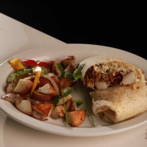 A plate with a halved burrito filled with meat and cheese, served in an authentic Mexican restaurant, accompanied by a side of sautéed bell peppers and diced potatoes, garnished with parsley