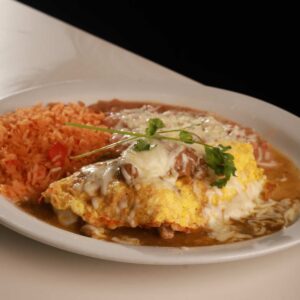 A plate of huevos rancheros with a fried egg topped with cheese and salsa, served alongside rice and beans, garnished with a sprig of cilantro at an authentic Mexican restaurant.