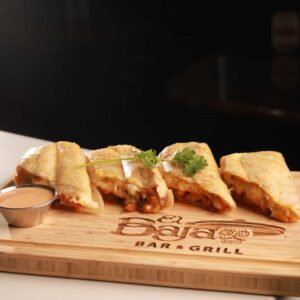 Sliced quesadilla served on a wooden board with a side of dipping sauce, garnished with cilantro, at "El Patio Mexican Restaurant.