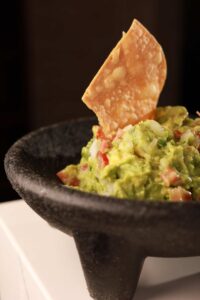 Fresh guacamole served in a black mortar with a crispy tortilla chip sticking out, set against a dark background at a restaurant.